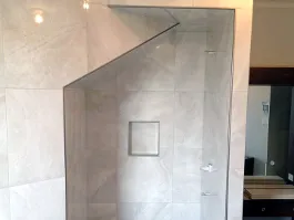 Douche vitrée recouverte de grands carreaux de céramique gris pâle, avec une niche murale